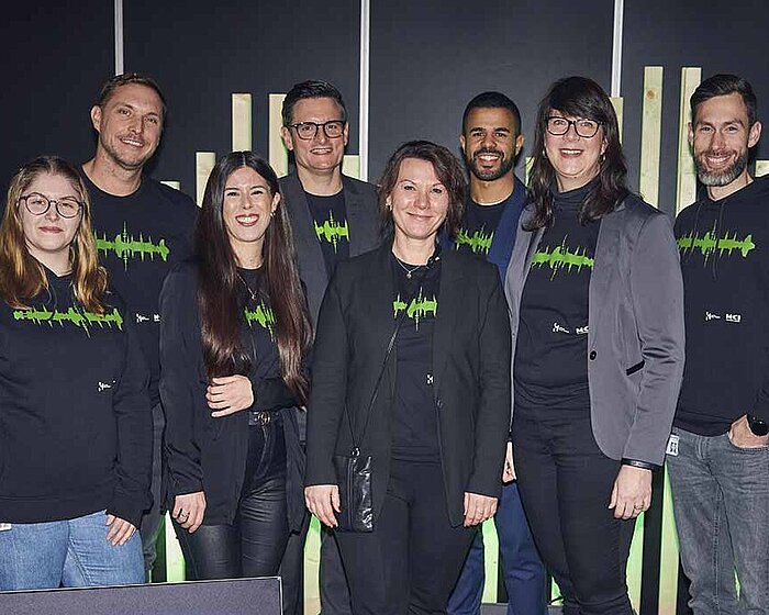 HAMBURG OPEN team. Eight women and men smile into the camera. In front of them there is a sign that says: HAMBURG OPEN.
