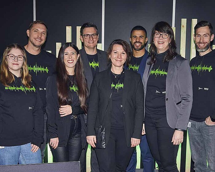 Team der HAMBURG OPEN. Acht Frauen und Männer lächeln in die Kamera. Vor ihnen steht ein Schild mit der Aufschrift: HAMBURG OPEN.