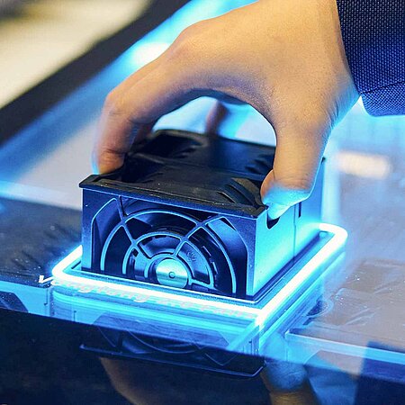 Hand setzt ein technisches Gerät in Form eines Würfels in ein leuchtendes Gehäuse ein.