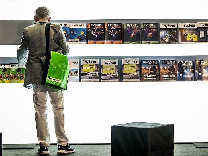 Person steht vor einer weißen Wand mit Fachpresse-Auslage.