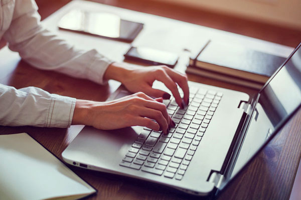 Laptop auf einem Schreibtisch, Frauenhände auf der Tastatur